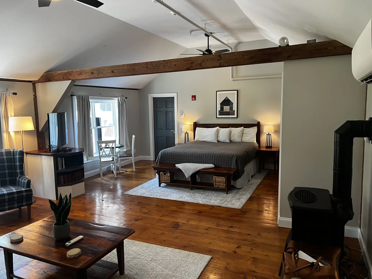 Interior room with pale walls, a vaulted white ceiling, exposed wooden beam and hardwood floor