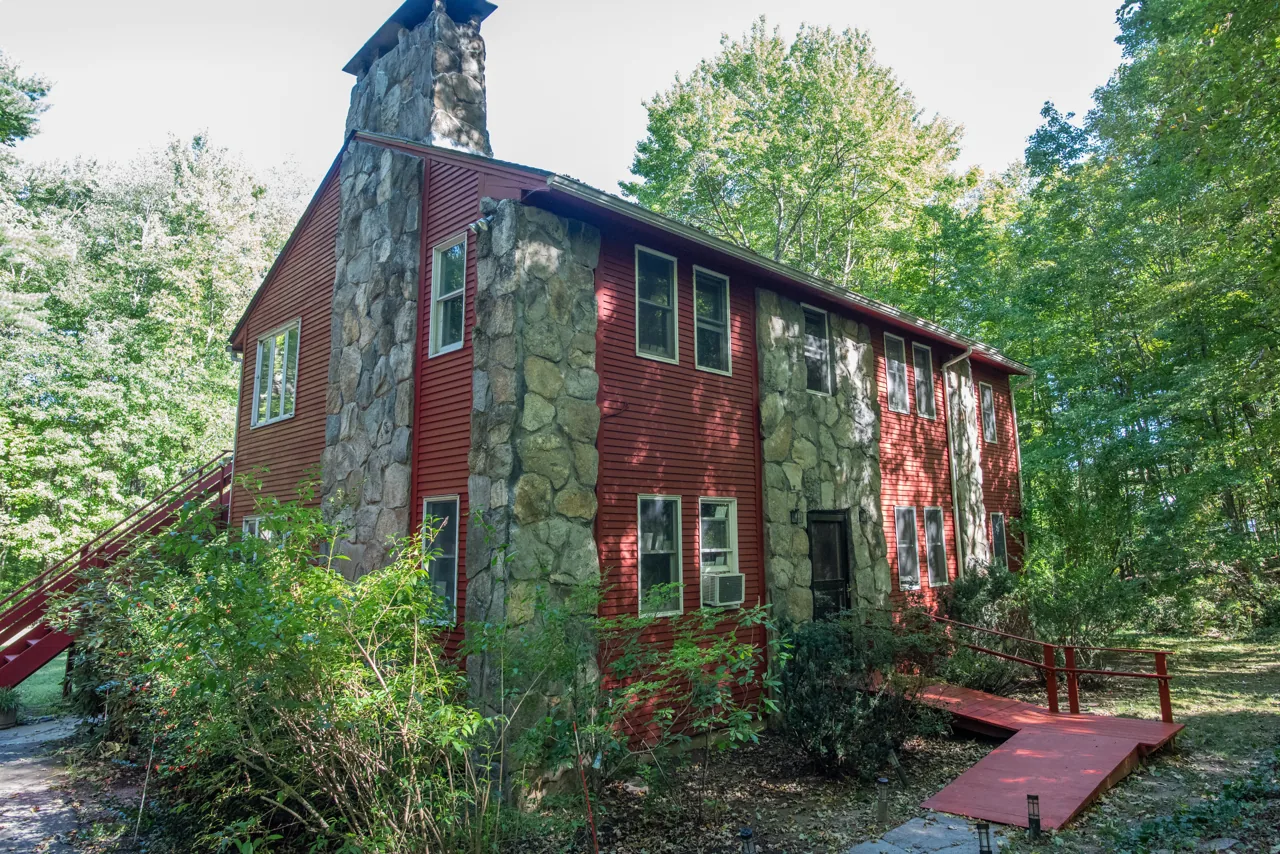 Red wood-sided home set among tall leafy trees
