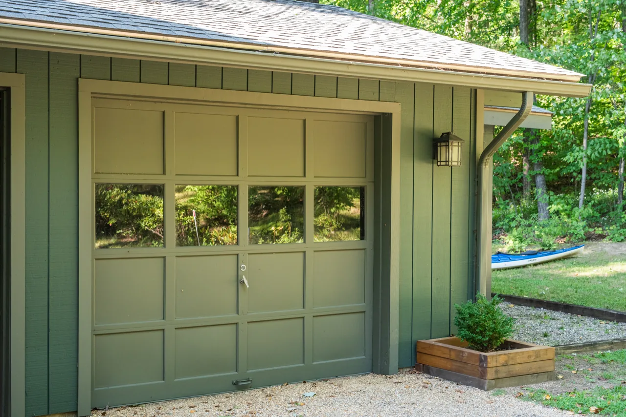 Sage green garage door and vertical siding beneath a porch roof