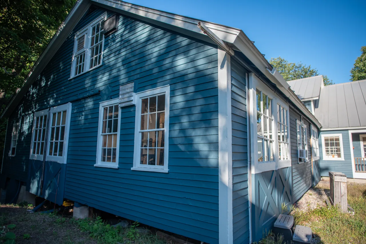 Blue exterior with a row of white-trimmed windows in dappled shade
