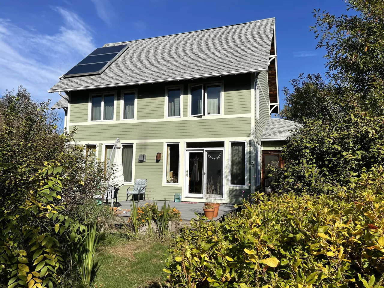 Sage green two-story home with white-trimmed windows, rooftop solar panels and garden