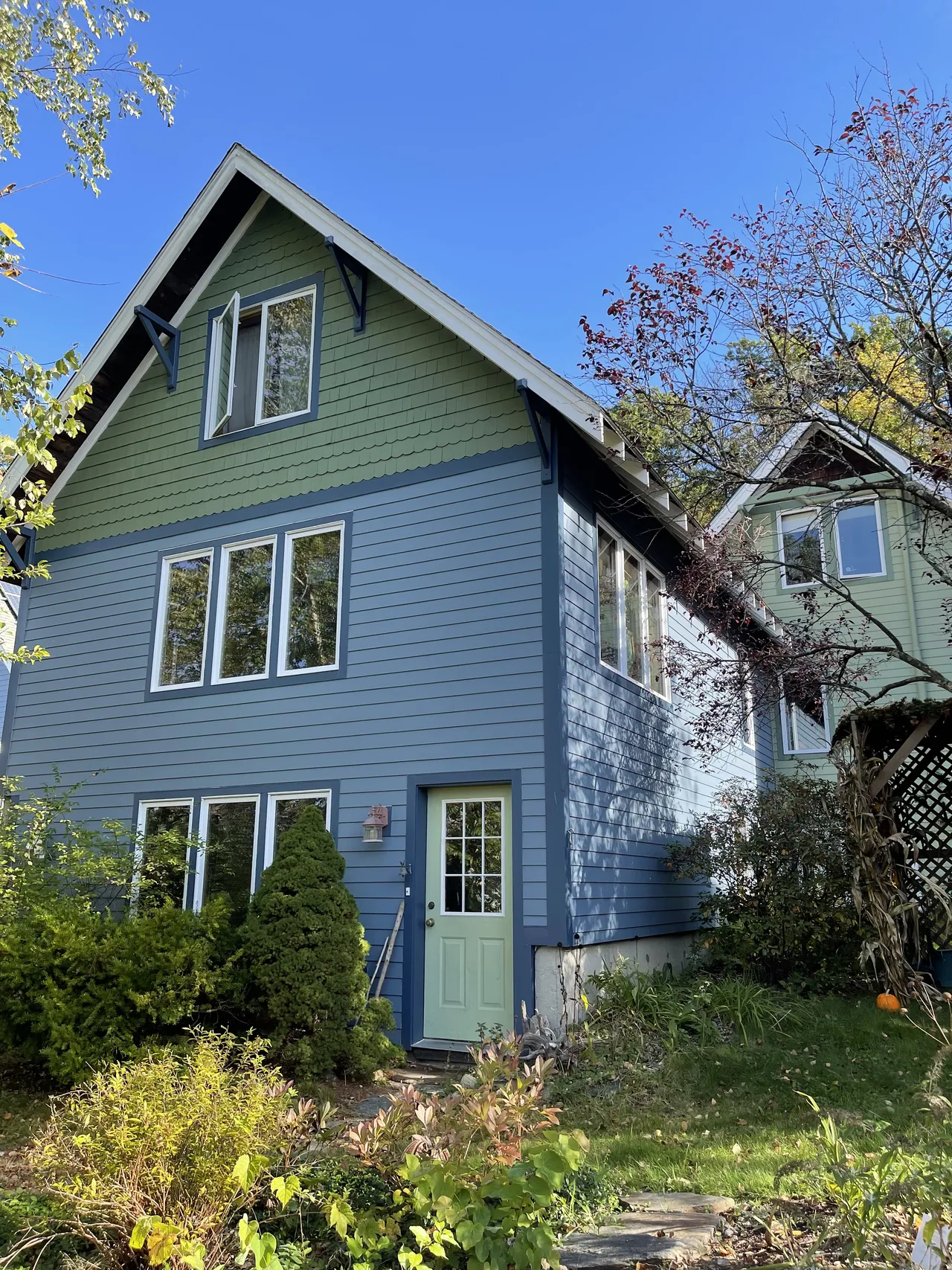 Two-tone house with blue lower siding, a green upper gable and white trim among trees